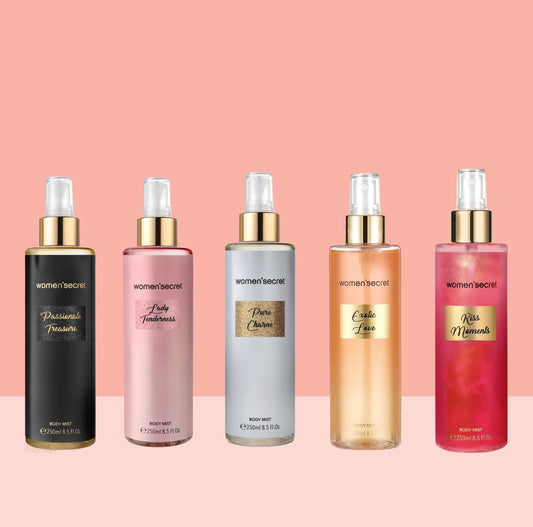 Four Woman Secret body spray bottles lined up against a pink background. The bottles are black, pink, silver, and peach, each with gold lettering and gold caps.